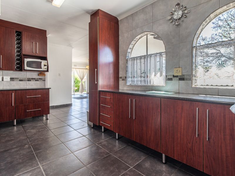 A well-maintained kitchen featuring dark wood cabinetry, granite countertops, tiled flooring, and distinctive arched windows that provide natural light.