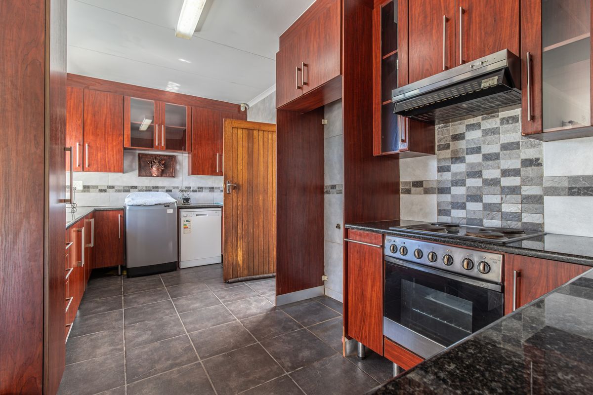 A functional kitchen featuring dark wood cabinetry, granite countertops, a built-in oven with hob, and tiled flooring with a mosaic backsplash.