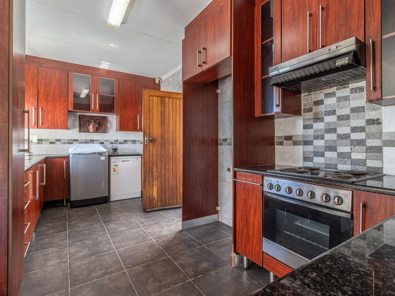 A functional kitchen featuring dark wood cabinetry, granite countertops, a built-in oven with hob, and tiled flooring with a mosaic backsplash.