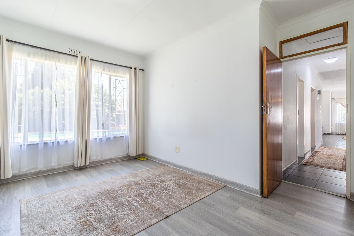 A bright, empty bedroom featuring modern laminate flooring, neutral walls, and a view through to the hallway.