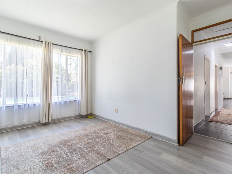 A bright, empty bedroom featuring modern laminate flooring, neutral walls, and a view through to the hallway.