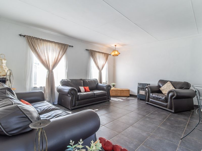 A spacious living room featuring dark tiled flooring and neutral walls, providing a functional and well-lit area for relaxation.