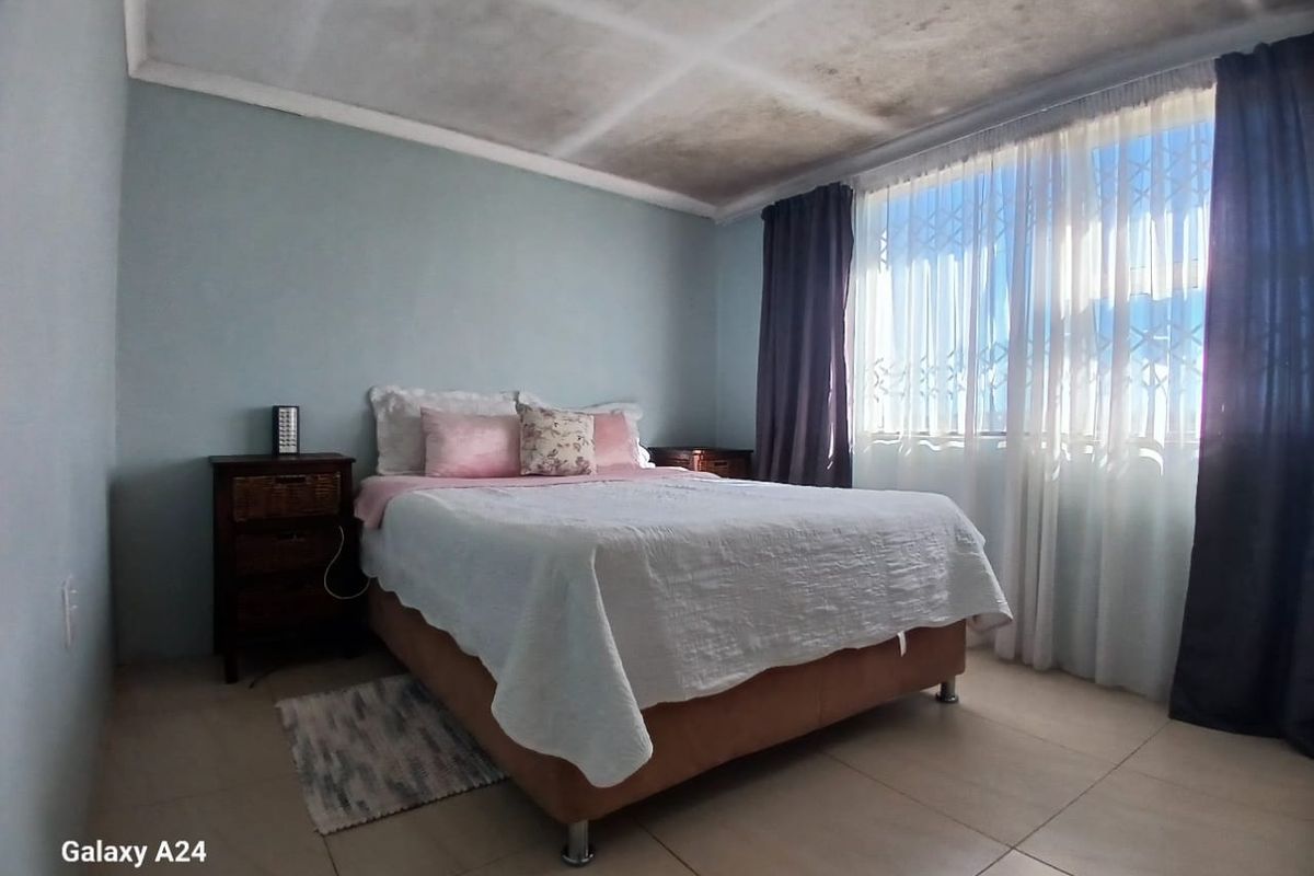 A bedroom featuring tiled flooring and a security gate on the window, with visible water staining on the ceiling requiring attention.