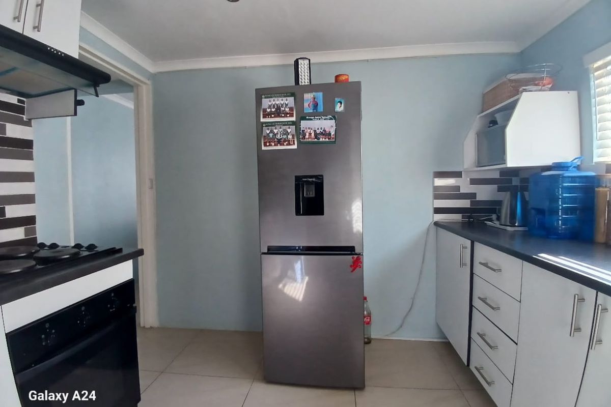 A functional kitchen featuring fitted white cabinetry, dark laminate countertops, built-in oven with hob, and tiled flooring.