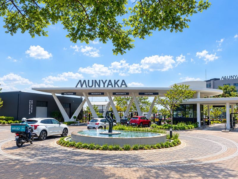 The main entrance and security gatehouse of the Munyaka estate, featuring a modern architectural design, paved driveway, and a central water fountain.