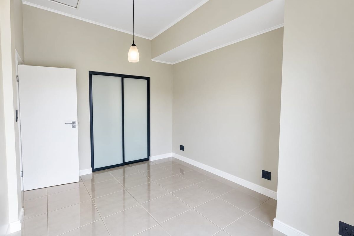 A bright, empty bedroom featuring neutral walls, tiled flooring, and a modern built-in sliding door wardrobe.