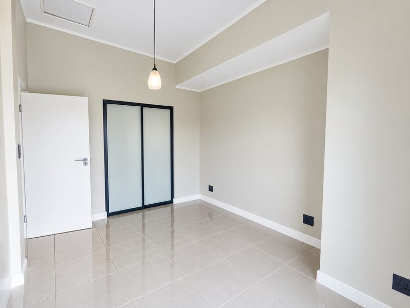A bright, empty bedroom featuring neutral walls, tiled flooring, and a modern built-in sliding door wardrobe.