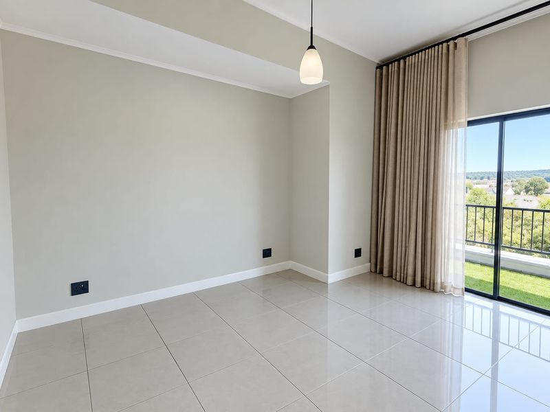 A bright, empty living area featuring polished tile floors, a modern pendant light, and a large sliding glass door leading to a balcony.