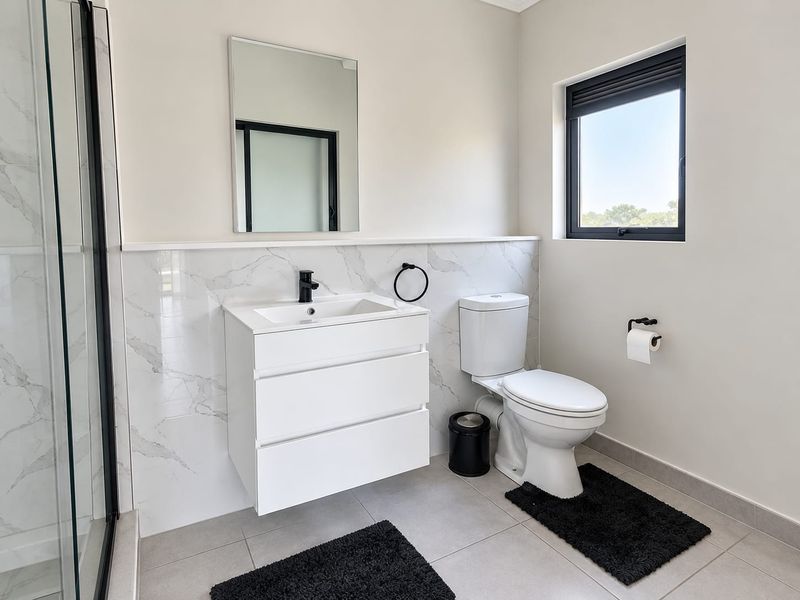 Modern bathroom featuring a wall-mounted vanity, marble-look tiled splashback, glass shower enclosure, and contemporary black fixtures.
