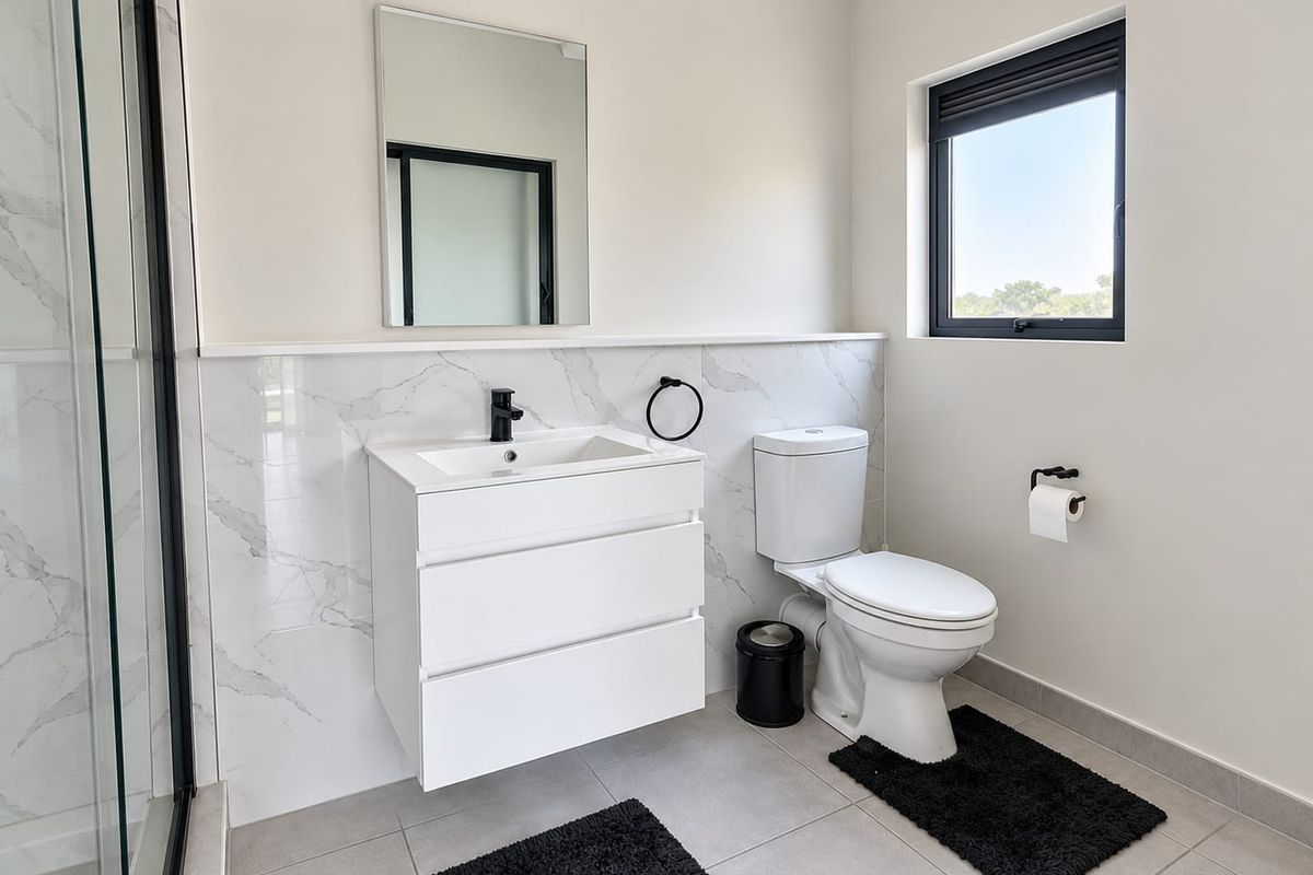 Modern bathroom featuring a wall-mounted vanity, marble-look tiled splashback, glass shower enclosure, and contemporary black fixtures.
