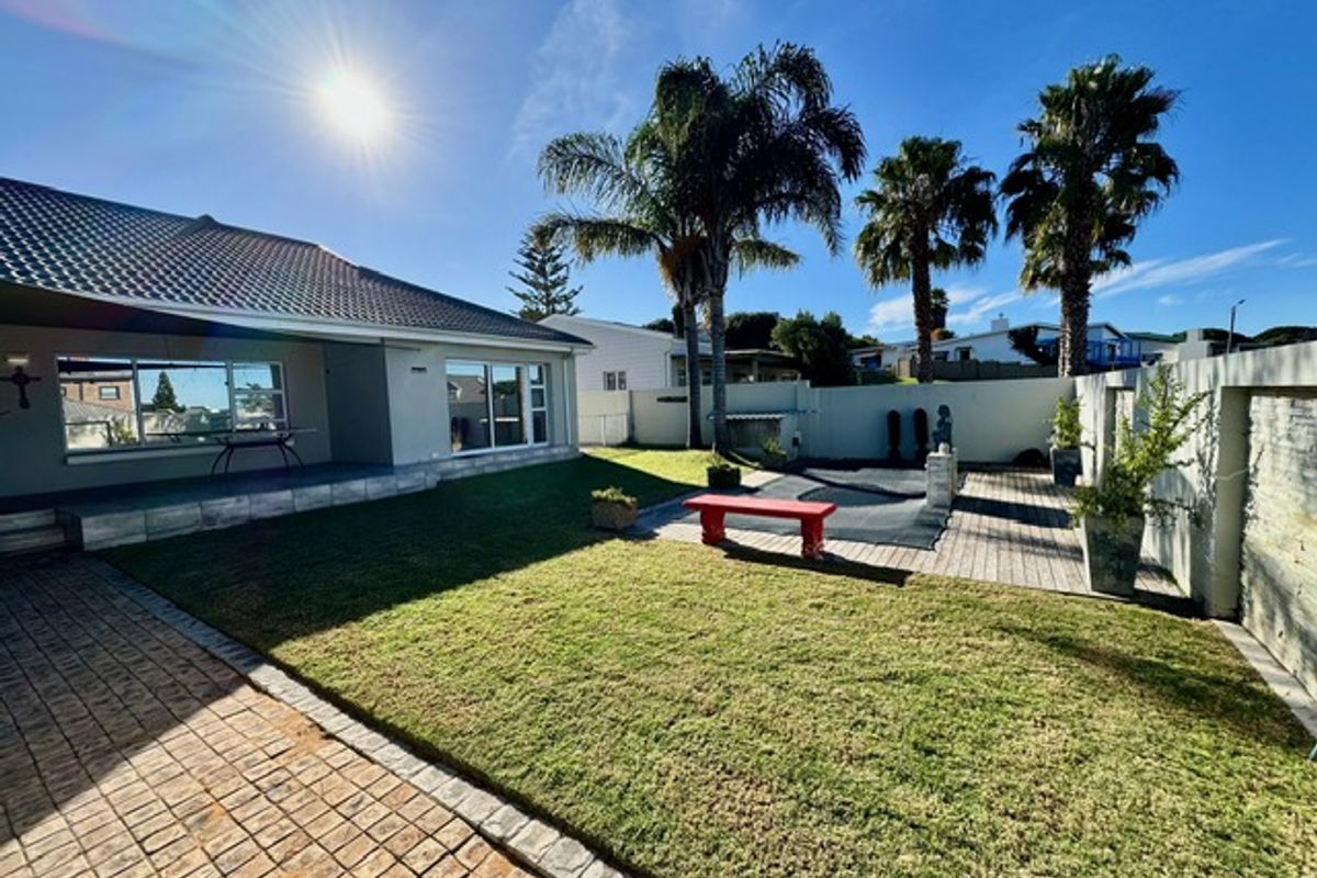 A spacious rear garden featuring a paved patio area, a well-maintained lawn, and established palm trees, providing a private outdoor living space.