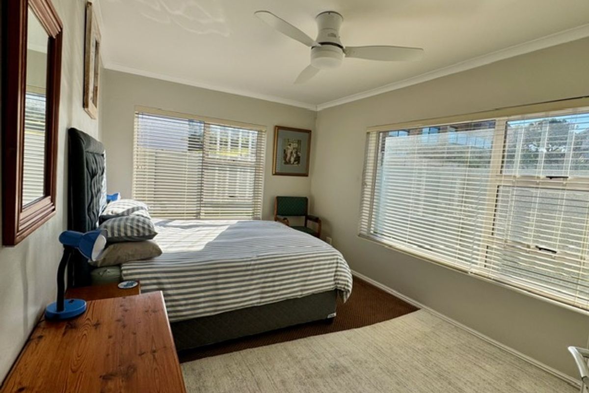 A bright bedroom featuring large windows with fitted blinds, a ceiling fan, and neutral wall finishes.