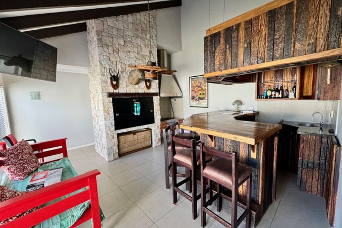 Spacious entertainment area featuring a stone-clad fireplace, vaulted ceilings with exposed beams, and a built-in wooden bar with integrated sink and shelving.