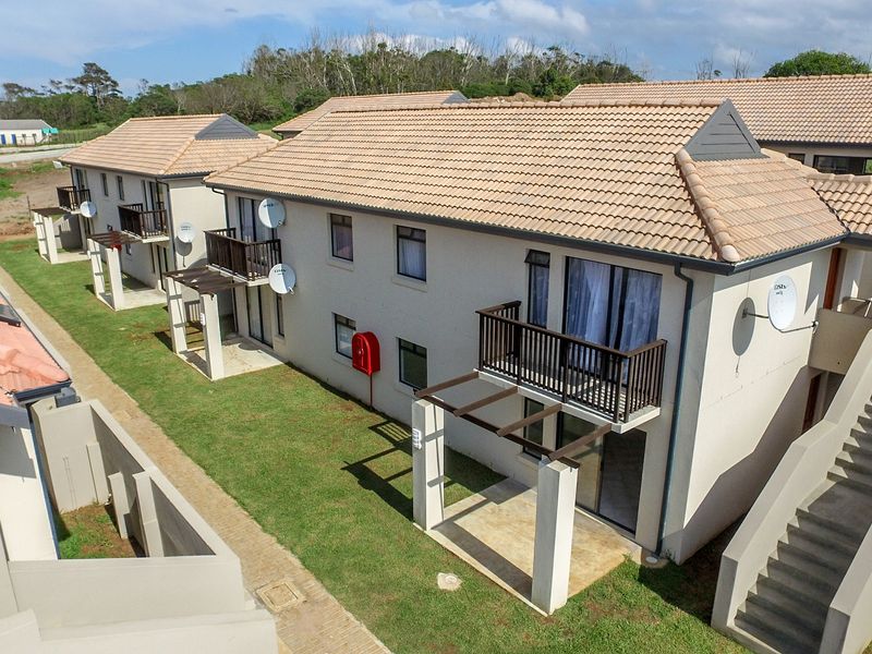 Aerial view of a modern apartment complex featuring tiled roofs, private balconies, ground-floor patios, and external staircases set within a landscaped residential estate.