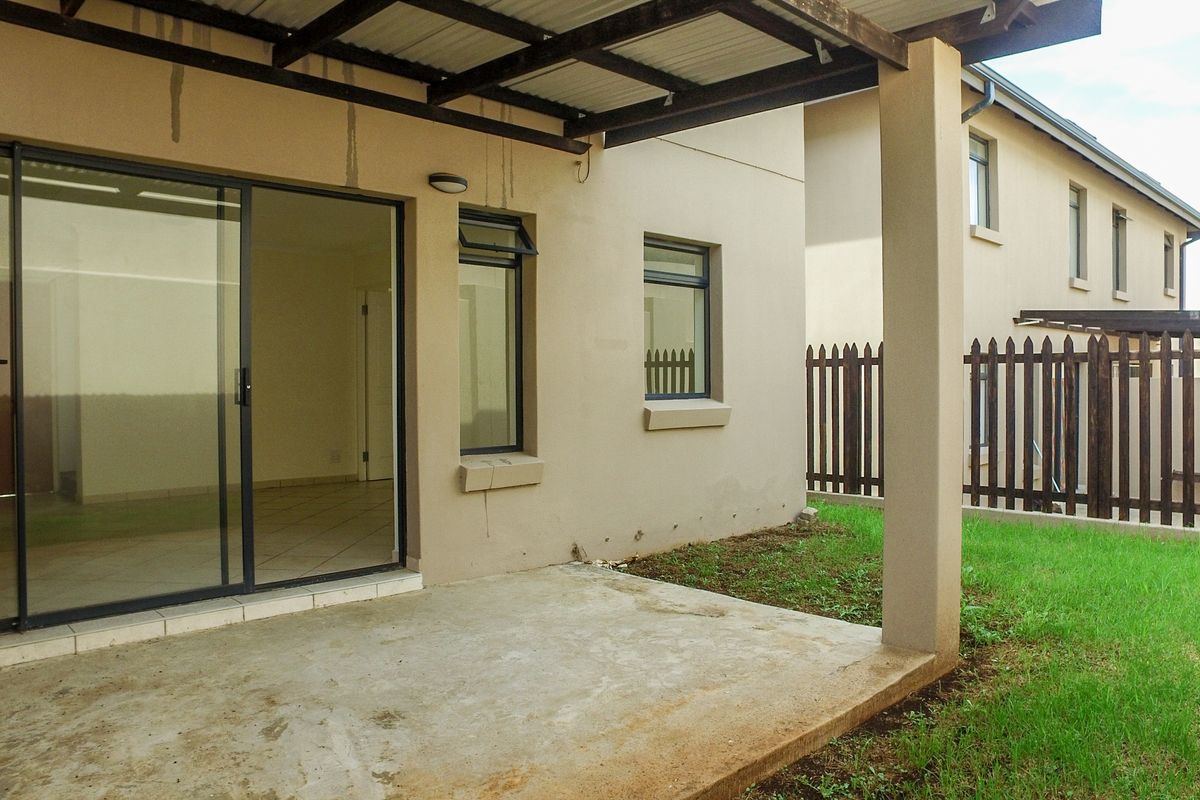A covered patio area featuring a concrete slab, sliding glass door access, and a timber pergola, overlooking a small private garden with timber fencing.