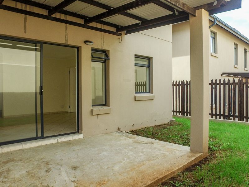 A covered patio area featuring a concrete slab, sliding glass door access, and a timber pergola, overlooking a small private garden with timber fencing.