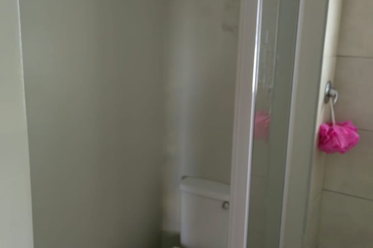 A compact bathroom featuring a toilet and a glass-enclosed shower with tiled walls, showing signs of wear and wall surface damage.