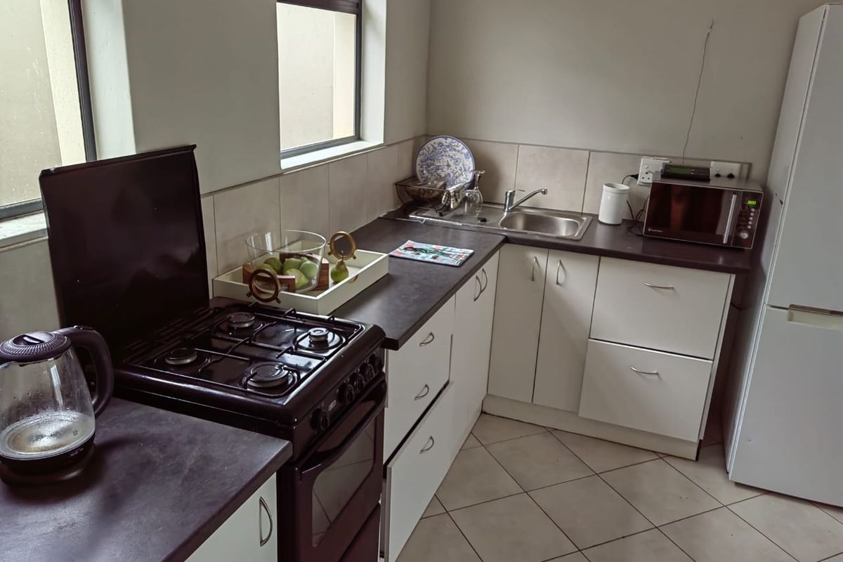 A functional kitchen featuring white cabinetry, dark laminate countertops, a stainless steel sink, and a gas stove with an oven.
