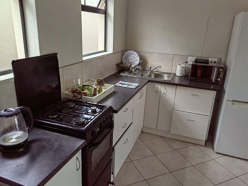 A functional kitchen featuring white cabinetry, dark laminate countertops, a stainless steel sink, and a gas stove with an oven.