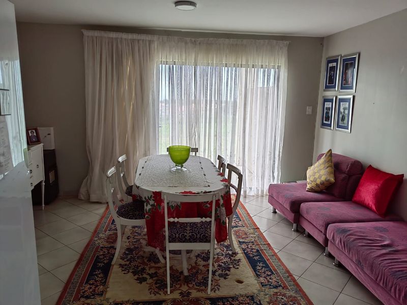 Open plan living and dining area featuring tiled flooring and a large sliding glass door with sheer curtains providing natural light.