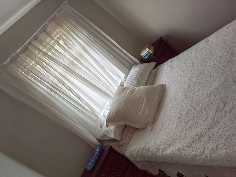 A bedroom featuring a window with installed curtain rails and sheer curtains.