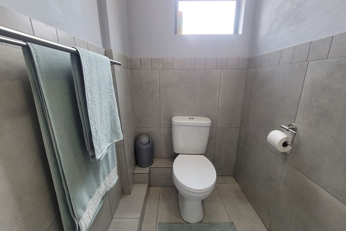 A clean and functional bathroom featuring neutral wall and floor tiling, a modern toilet, and fixed bathroom accessories.