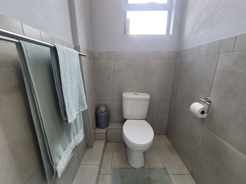 A clean and functional bathroom featuring neutral wall and floor tiling, a modern toilet, and fixed bathroom accessories.