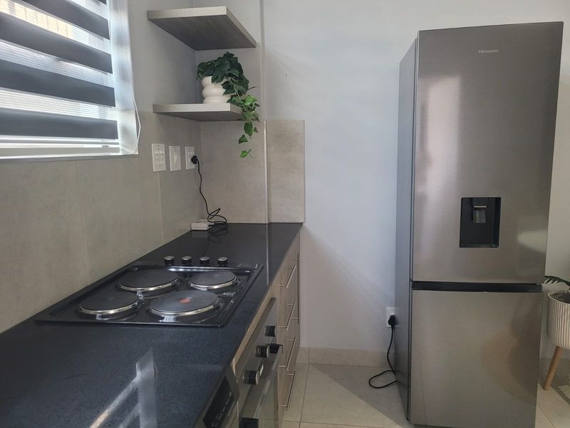 Modern kitchen featuring sleek granite countertops, a built-in hob and oven, floating shelving, and contemporary tiled splashbacks.