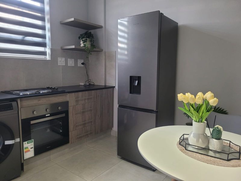 Modern kitchen featuring sleek laminate cabinetry, stone countertops, built-in oven, hob, and stylish floating shelves, complemented by neutral tiled flooring and contemporary finishes.