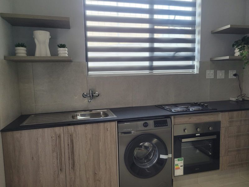 Modern kitchen featuring wood-grain cabinetry, integrated oven and hob, stainless steel sink, and sleek tiled splashback with floating shelving.