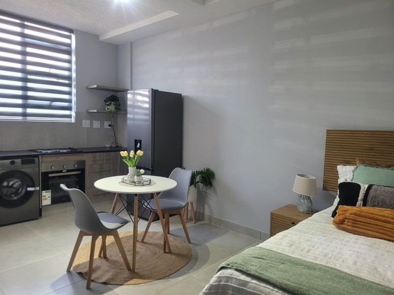 A modern open-plan studio apartment featuring a compact kitchen with built-in appliances, sleek cabinetry, and a combined living and sleeping area.