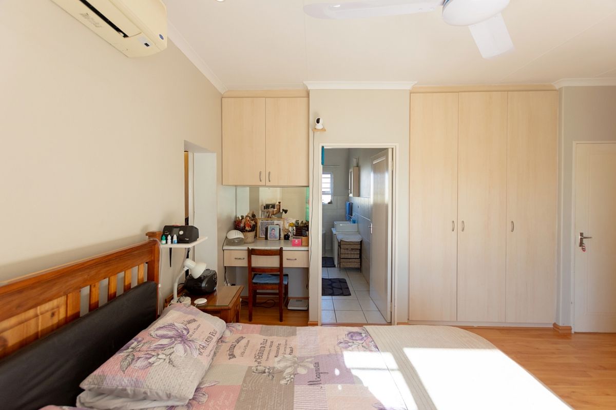 Bedroom featuring laminate flooring, built-in cupboards, a vanity area, and an en-suite bathroom access, equipped with a ceiling fan and air conditioning unit.