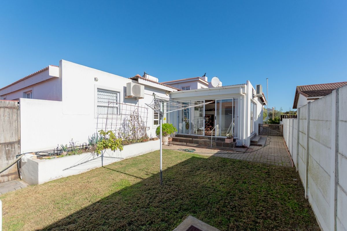 Rear exterior view of the property featuring a paved patio, small lawn area, raised planter beds, and sliding door access to the main dwelling.