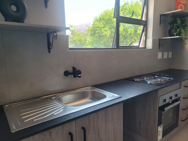 Modern kitchen featuring a stainless steel sink, black wall-mounted tap, built-in electric hob, oven, and contemporary laminate cabinetry with open shelving.