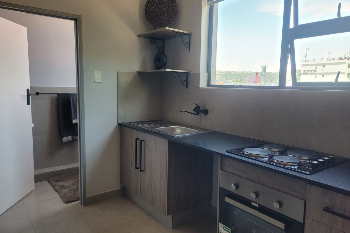 Modern compact kitchen featuring wood-finish cabinetry, integrated electric hob and oven, stainless steel sink, and large window with natural light.