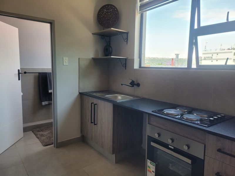 Modern compact kitchen featuring wood-finish cabinetry, integrated electric hob and oven, stainless steel sink, and large window with natural light.