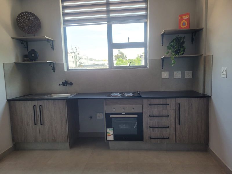 Modern kitchen featuring wood-look cabinetry, dark stone countertops, built-in oven, electric hob, and a tiled backsplash with floating shelving.