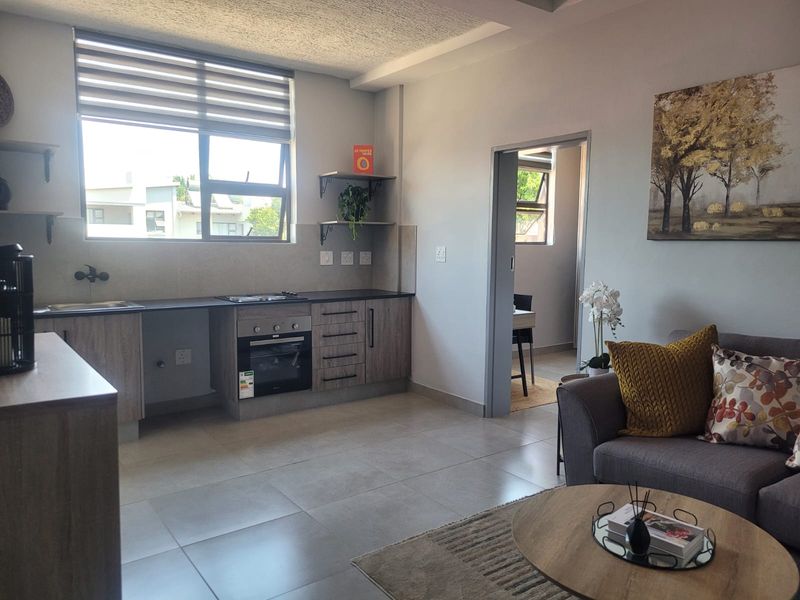 An open-plan living and kitchen area featuring modern cabinetry, built-in oven and hob, tiled floors, and neutral finishes throughout.