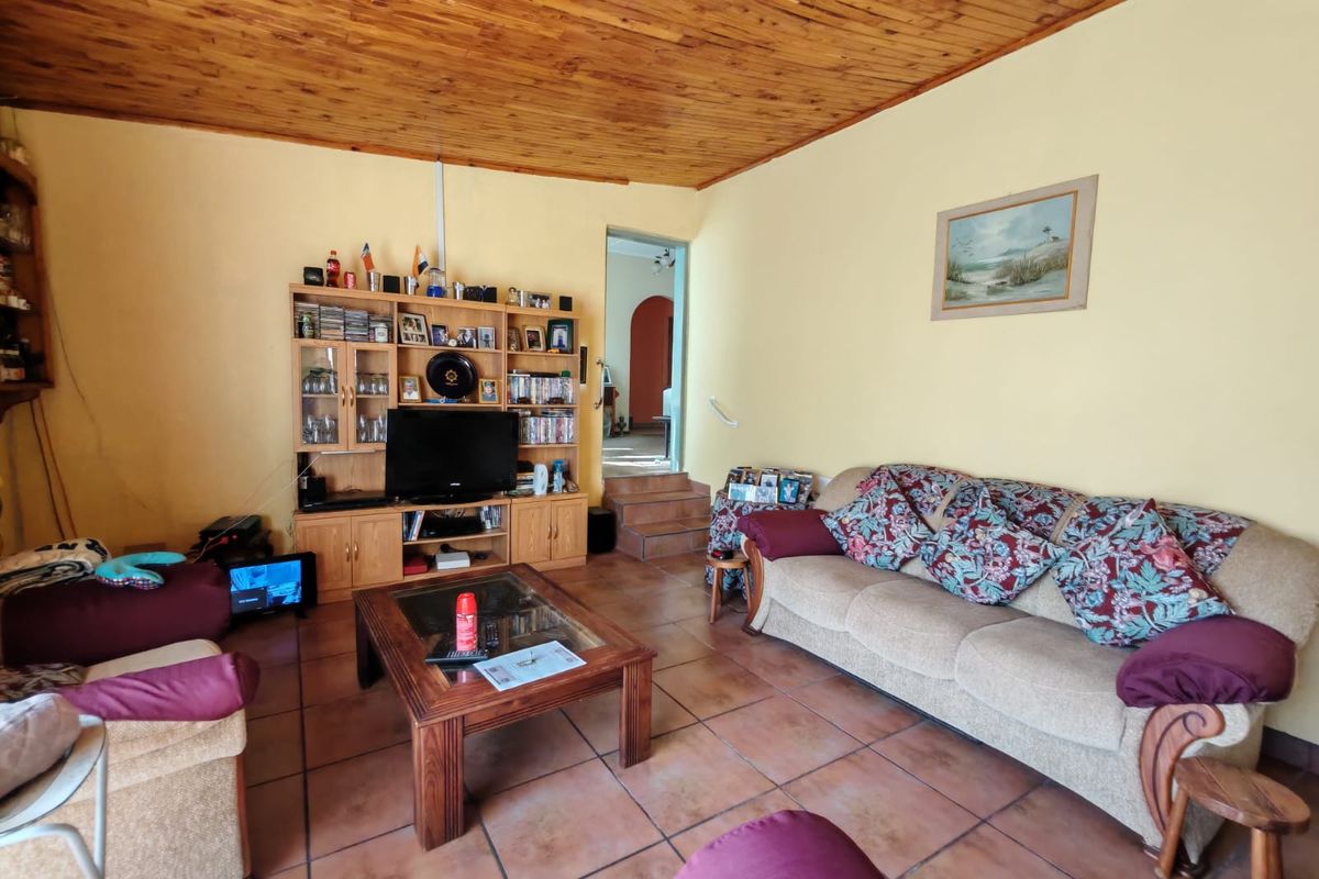 A living room featuring terracotta floor tiles and a timber-clad ceiling, with a built-in shelving unit and access to an adjacent room via steps.