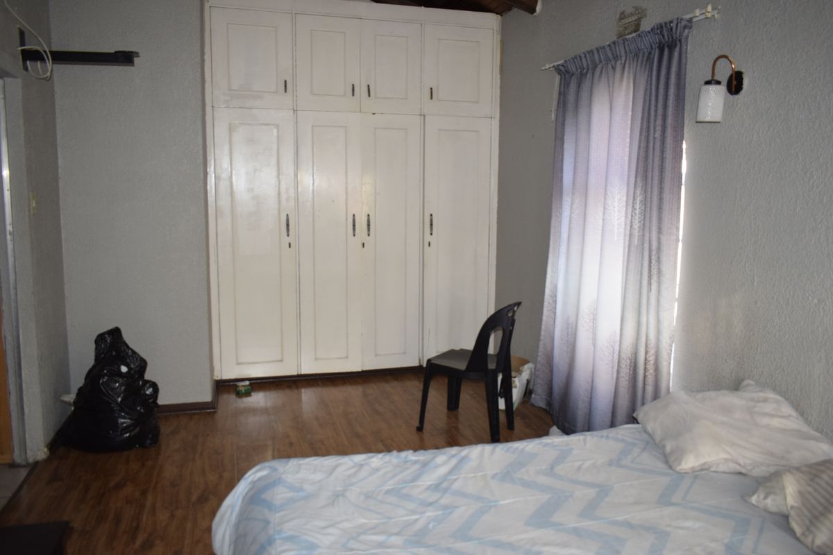 A bedroom featuring built-in cupboards, laminate flooring, and a wall-mounted light fixture, offering a functional space with potential for cosmetic updates.