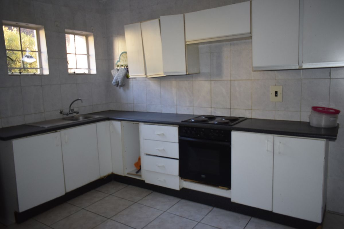 A dated kitchen featuring white cabinetry, dark countertops, and a built-in oven and hob, requiring cosmetic updates to improve functionality and aesthetic appeal.