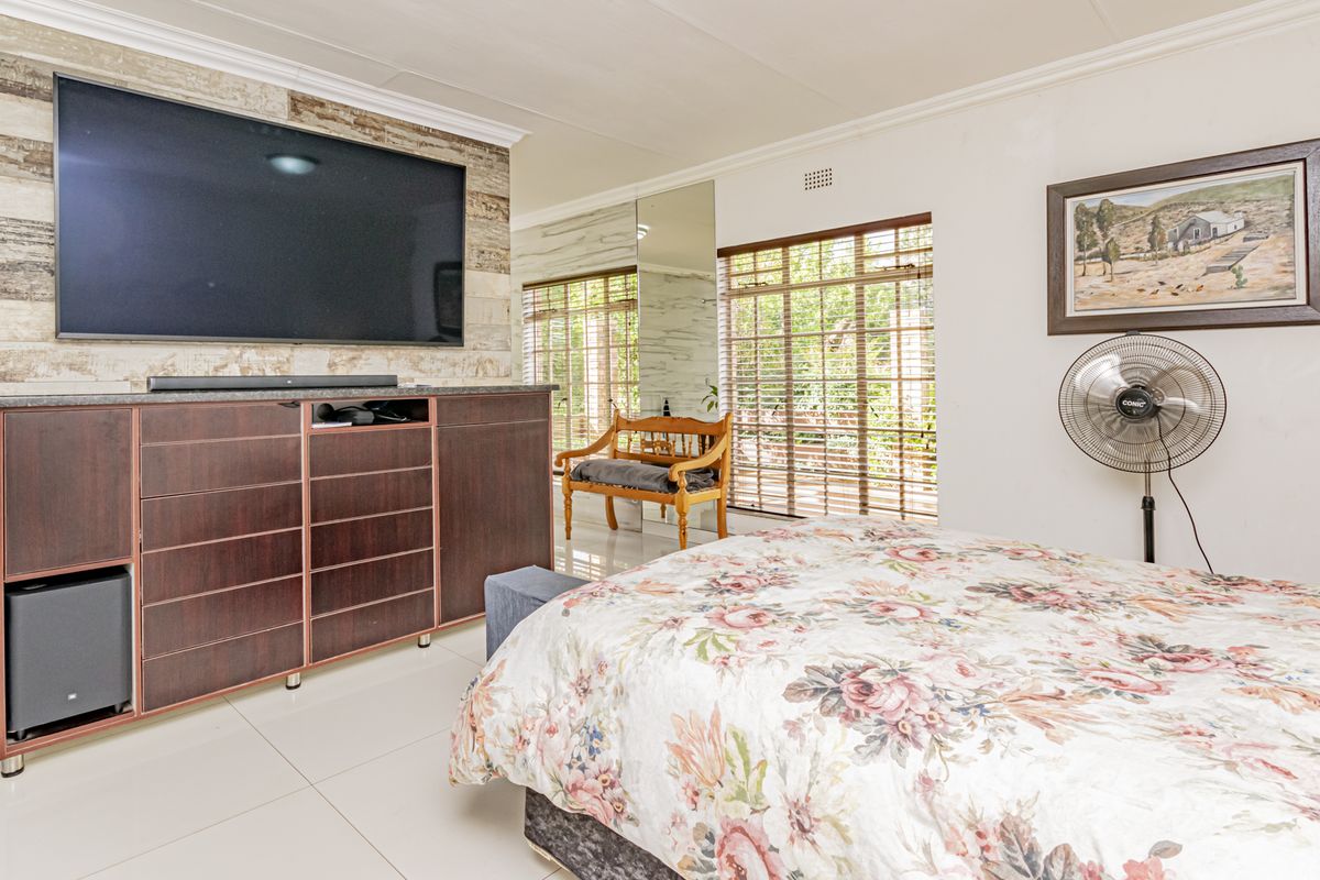 A well-maintained bedroom featuring tiled flooring, a wood-look feature wall, and large windows with venetian blinds.