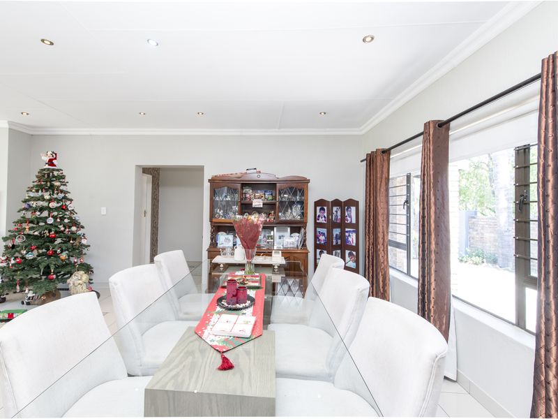A bright dining room featuring tiled flooring, recessed ceiling lighting, and large windows with curtain tracks, providing a functional space for family meals.