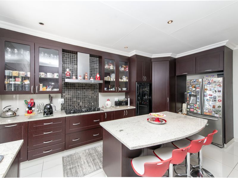 Modern kitchen featuring dark wood cabinetry, granite countertops, a central island with breakfast bar seating, and a tiled backsplash with a built-in extractor fan.