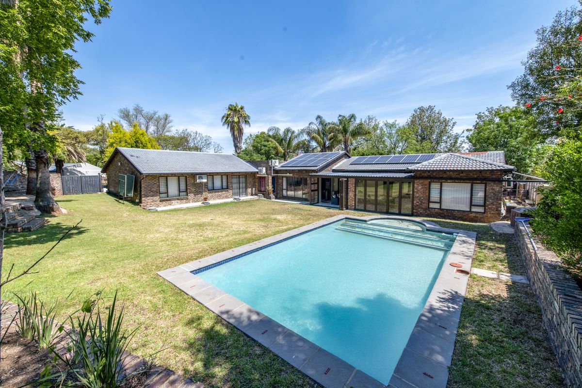 Spacious rear garden featuring a large swimming pool, brick-faced exterior, and solar panels installed on the tiled roof.
