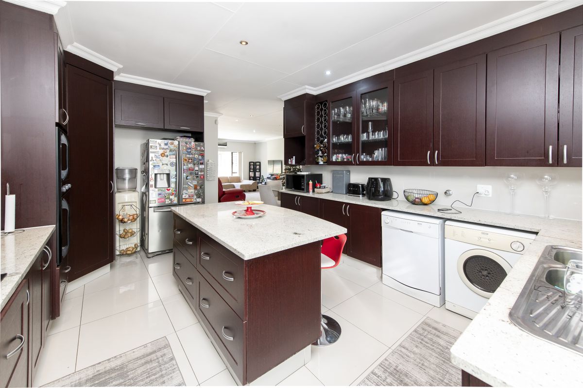 A spacious kitchen featuring dark wood cabinetry, granite countertops, a central island, and integrated space for laundry appliances.