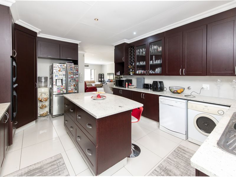 A spacious kitchen featuring dark wood cabinetry, granite countertops, a central island, and integrated space for laundry appliances.