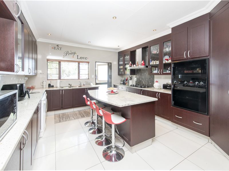 Spacious kitchen featuring dark wood cabinetry, granite countertops, a central island with breakfast bar seating, and built-in oven and hob.