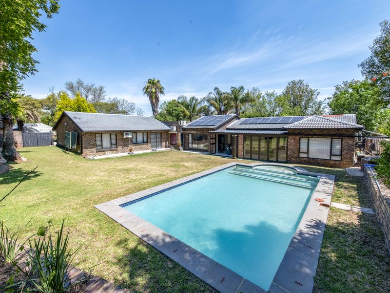 Spacious rear garden featuring a large swimming pool, brick-faced exterior, and solar panels installed on the tiled roof.