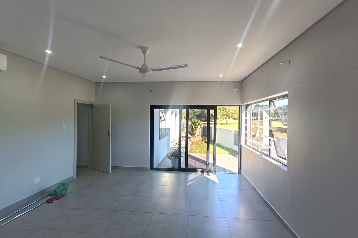 A bright, empty living room featuring neutral tiled flooring, recessed lighting, a ceiling fan, and sliding glass doors leading to an outdoor area.